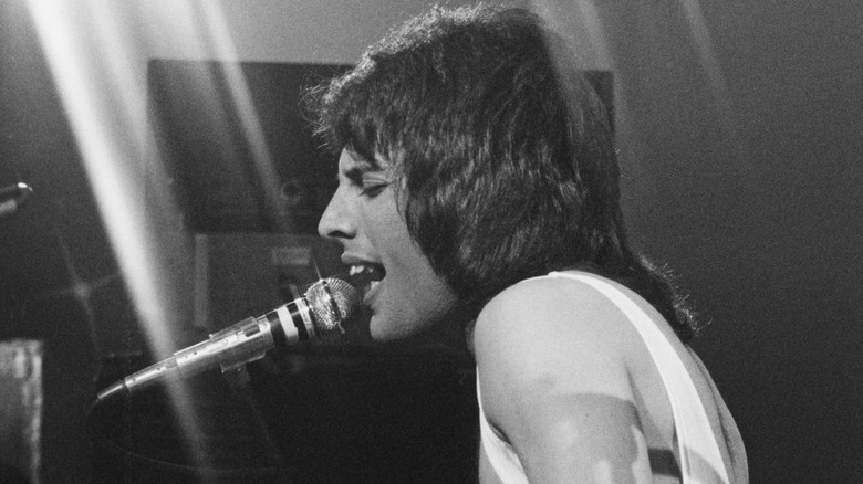 Freddie Mercury singing into a microphone while playing piano