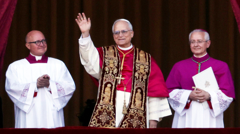 Pop Leo XIV waving from balcony with two clerics