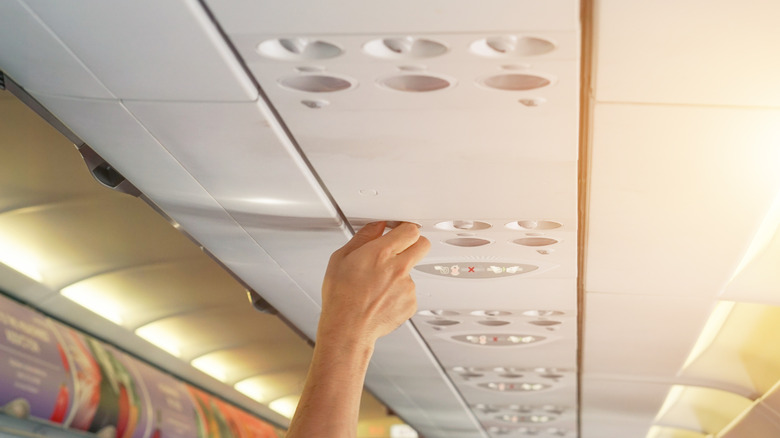 Hand adjusting overhead vent on airplane