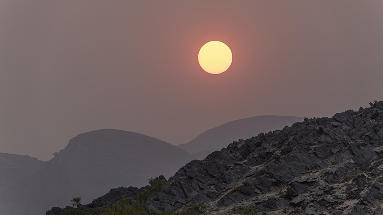 sun behind dusty clouds, rocky ridges in foreground