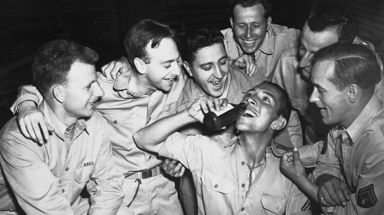 Laughing soldiers watching another soldier pour a beer in his mouth