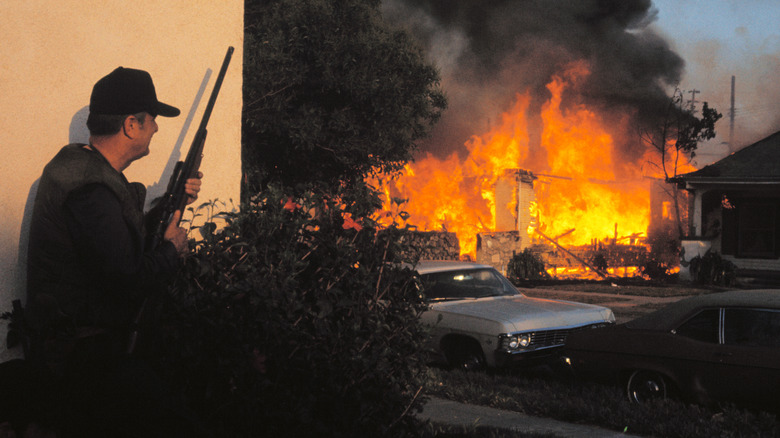 An officer with a long gun watching the SLA safehouse burn