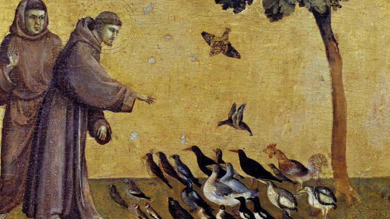 Saint Francis in robe raising hand towards group of sitting birds